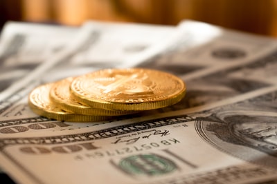Tři kulaté zlaté mince na 100 amerických dolarových bankovkách